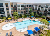 Thumbnail 1 of 49 - Luxury Apartments in Decatur, GA - Reserve Decatur - Saltwater Swimming Pool with In-Pool and Poolside Lounge Seats, Tables and Chairs with Umbrellas, Trees, and Manicured Shrubs.