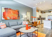 Thumbnail 19 of 49 - Two-Bedroom Luxury Apartments in Decatur, GA - Reserve Decatur - Open Layout Living Room with Designer Plank Flooring, Area Rug, Sectional Couch, Coffee Table, Wall Art, Standing Lamp, and View of Dining Area and Kitchen.