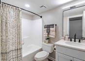 Thumbnail 16 of 25 - A bathroom with a white toilet, a white sink, and a shower curtain.