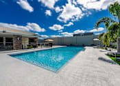Thumbnail 1 of 25 - A large outdoor swimming pool with a concrete floor and a concrete wall on the right side.
