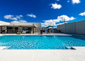 Thumbnail 19 of 25 - A large swimming pool in front of a building with a blue sky and clouds in the background.