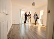 Thumbnail 44 of 53 - Three people are standing in a room with wooden floors and white walls.