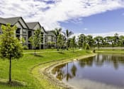 Thumbnail 30 of 32 - A serene landscape with a pond, a tree, and a row of houses.