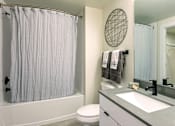 Thumbnail 20 of 30 - A bathroom with a white shower curtain, a round mirror, and a white toilet at Saba Pompano Beach, Pompano Beach, 33062
