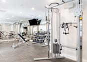 Thumbnail 9 of 16 - A gym with a variety of equipment including a weight bench, a cable machine, and a flat screen TV.
