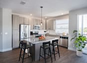 Thumbnail 9 of 34 - One-Bedroom Apartments in Maitland - The Parker at Maitland Station - Kitchen with Wood Vinyl Plank Flooring, Tan Flat-Panel Cabinetry, Granite Countertops, Stainless Steel Appliances, Kitchen Island with Seating, and Pendant Light.