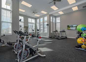 Thumbnail 8 of 30 - A gym with a row of stationary bikes and a fan.