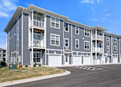 Thumbnail 50 of 51 - A large grey apartment building with a parking lot in front.