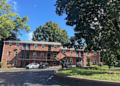 Thumbnail 23 of 24 - A red brick apartment building with cars parked in front.
