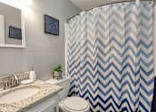 Thumbnail 9 of 20 - A bathroom with a sink, toilet, and a shower curtain with a chevron pattern.