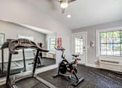Thumbnail 11 of 20 - A room with a treadmill, a stationary bike, and a mirror.