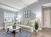 Thumbnail 5 of 20 - Two-Bedroom Apartments in Riverview, FL - Sherwood Oaks Apartments - Open Living Room With Plush Sofa, Patterned Area Rug, Coffee Table, Large Window Blinds, and Modern Floor Lamps.