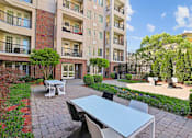 Thumbnail 26 of 39 - Atlanta, GA, Luxury Apartments Near Lenox Square - The Rocca - A Patio with Tables and Chairs and Paved Walkways Lined with Shrubs.