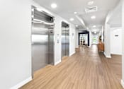 Thumbnail 22 of 30 - A long hallway with wood floors and two elevators.