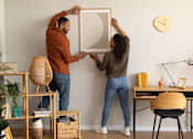 Thumbnail 8 of 28 - a man and a woman are hanging a mirror on a wall