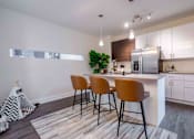 Thumbnail 7 of 22 - Studios in Tampa, FL - Society Westshore - Kitchen with Wood Plank Style Flooring, Large Island with Seating, Pendant Lights, Quartz Countertops, Stainless Steel Appliances, and Flat-Panel Cabinetry.