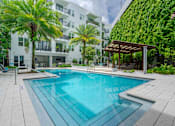 Thumbnail 17 of 22 - A swimming pool surrounded by a white building and palm trees.