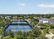 Thumbnail 32 of 35 - A tennis court surrounded by greenery and buildings.