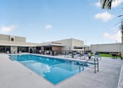 Thumbnail 18 of 35 - A large swimming pool is surrounded by a concrete patio and a building.