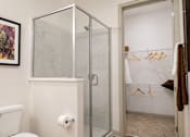 Thumbnail 23 of 40 - A bathroom with a toilet, a shower with a glass door, and a towel hanging on a rack.