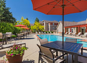 Thumbnail 19 of 37 - A poolside table with chairs and an umbrella overlooking a pool.