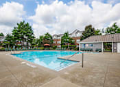 Thumbnail 27 of 29 - A large outdoor swimming pool surrounded by a concrete patio and a metal fence.