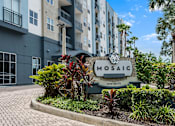 Thumbnail 1 of 35 - A sign for Mosaic Apartments is in front of a building with a landscaped area.
