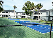 Thumbnail 27 of 30 - A tennis court surrounded by a fence and palm trees.