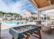 Thumbnail 54 of 56 - A foosball table is in the middle of a patio with a pool and houses in the background.
