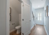 Thumbnail 23 of 56 - A white toilet in a small bathroom with a door open to a hallway.