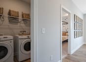 Thumbnail 52 of 56 - A laundry room with a washer and dryer and a doorway leading to a living room.