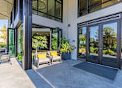 Thumbnail 26 of 27 - A modern building entrance with glass doors and a bench with yellow cushions.