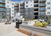 Thumbnail 15 of 26 - A courtyard with a fire pit and seating area in front of apartment buildings.