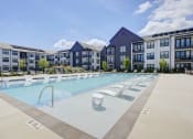 Thumbnail 28 of 28 - Dog-Friendly Apartments in Huntsville, AL - The Collins - Resort-Style Salt Water Pool with Spacious Sundeck, Submerged and Poolside Lounge Seats, and View of Apartment Buildings.