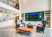 Thumbnail 14 of 28 - Huntsville, AL Luxury Apartments - The Collins - Clubhouse with Wingback Armchairs, Leather Bench, Coffee Table, Wall-Mounted TV, Extensive Shelving, and Pendant Lights.