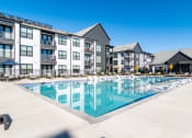 Thumbnail 26 of 28 - Dog-Friendly Apartments In Huntsville, AL - The Collins - Gated Resort-Style Salt Water Pool with Poolside and Submerged Lounge Seats, Tables, Chairs, Umbrellas, and View of Apartment Buildings