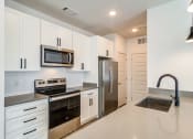 Thumbnail 2 of 28 - Pet-Friendly Apartments in Huntsville, AL - The Collins - Gourmet Kitchen with Quartz Countertops, Stainless Steel Appliances, Custom Designer Cabinetry, Tile Backsplash, and Pendant Lights.