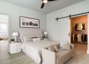 Thumbnail 7 of 28 - Huntsville, AL Luxury Apartments for Rent - The Collins - Bedroom with Wood-Style Flooring, White Walls, Large Bed, Nightstands with Lamps, Settee Bench, Ceiling Fan, and Spacious Closet.