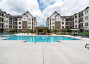 Thumbnail 50 of 56 - a swimming pool with chaise lounge chairs and umbrellas in front of an apartment building