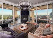 Thumbnail 2 of 44 - Three-Bedroom Luxury Apartments in Buckhead, GA - The Huntley - Lounge Area with Glass Walls, Couches, Stools, Large Coffee Table, Stylish Light Fixture, Gas Fire Place, and Access to Outdoor Terrace.