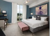 Thumbnail 21 of 44 - Dog-Friendly Luxury Apartments in Buckhead, GA - The Huntley - Spacious Bedroom with Carpet Flooring, Large Bed, Footboard Bench, Nightstand with Lamp, Desk, Armchair, Wall Art, Ceiling Fan, and Floor-to-Ceiling Window.