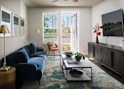 Thumbnail 3 of 31 - Pet-Friendly Luxury Apartments in Panama City, FL - The Kelly at 23rd - Living Room with Vinyl Wood-Inspired Plank Flooring, Area Rug, Blue Couch, Side Tables with Lamps, Coffee Tables, Orange Chair, Storage Cabinet, Wall-Mounted TV, Ceiling Fan, Window, and Glass Door with Access to Private Patio.