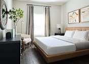 Thumbnail 4 of 31 - Panama City, FL Pet-Friendly Luxury Apartments - The Kelly at 23rd - Bedroom with Vinyl Wood-Inspired Plank Flooring, Queen-Size Bed, Nightstand with Lamp, Dresser, Wall-Mounted Round Mirror, Armchair, Floor Lamp, and Large Window.