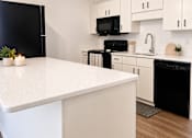 Thumbnail 2 of 15 - A kitchen with black appliances and white countertops.