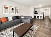 Thumbnail 4 of 15 - A living room with a grey couch, a coffee table, and a bar area in the background.