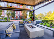 Thumbnail 17 of 27 - A patio with a couch and a bench with a fire pit in the middle.