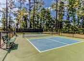 Thumbnail 32 of 47 - A tennis court surrounded by a fence and trees.