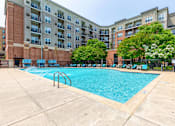 Thumbnail 17 of 20 - an outdoor swimming pool with chaise lounge chairs and an apartment building in the background