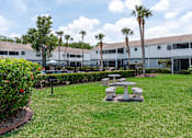 Thumbnail 23 of 25 - A white building with a black fence and a green lawn with a picnic table.