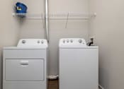 Thumbnail 19 of 49 - A laundry room with two washing machines and a shelf above them.